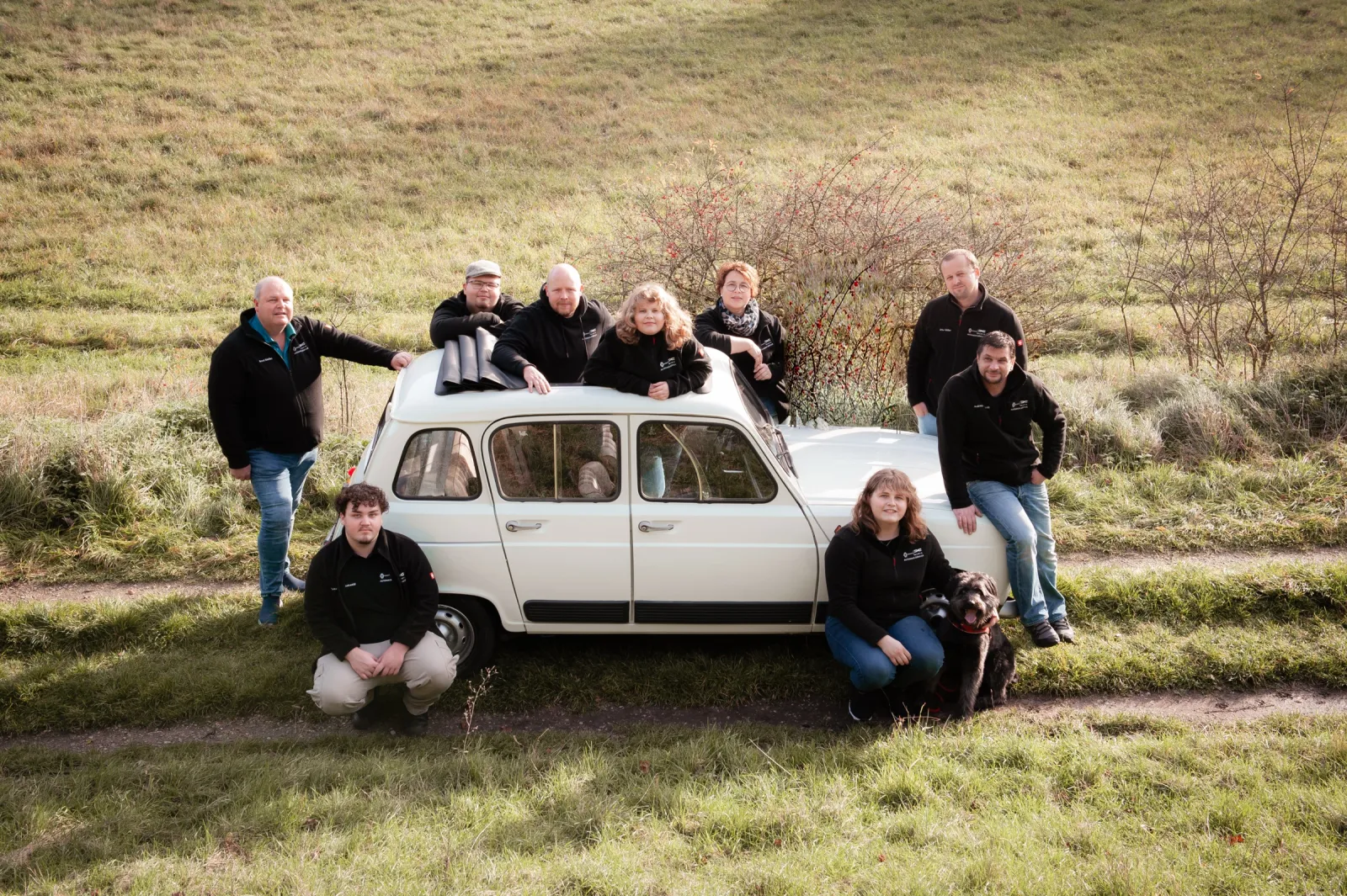 Das Team des Autohauses Dörfler mit Hund an einem weißen Renault R4 auf einer Wiese